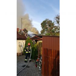zdjęcie przedstawia płonący dach i strażaków gaszących pożar