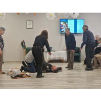 Osoby starsze obserwujące pokaz udzielania pierwszej pomocy przez funkcjonariuszy